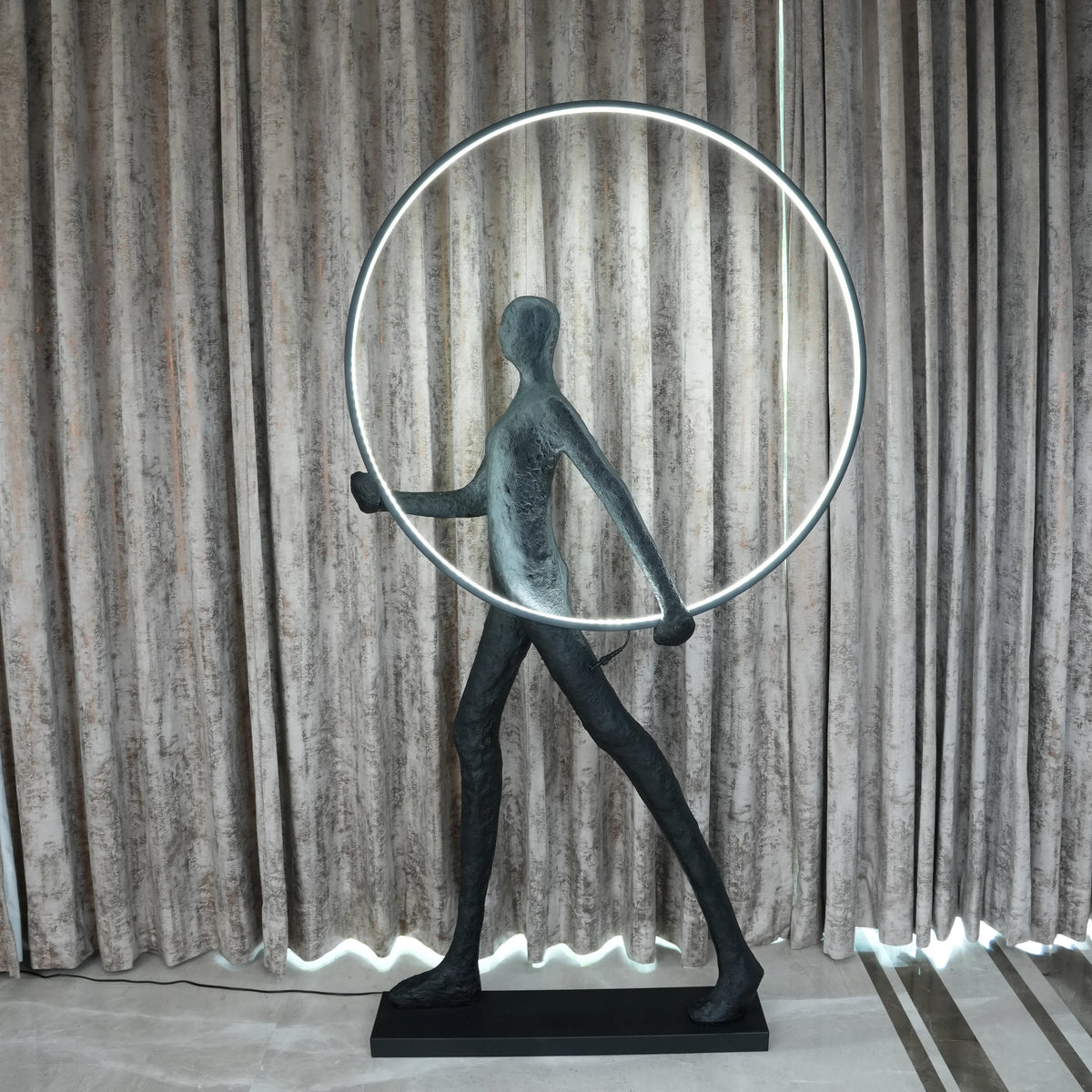 Decorative sculpture of a figure with a circular light feature against a curtain background