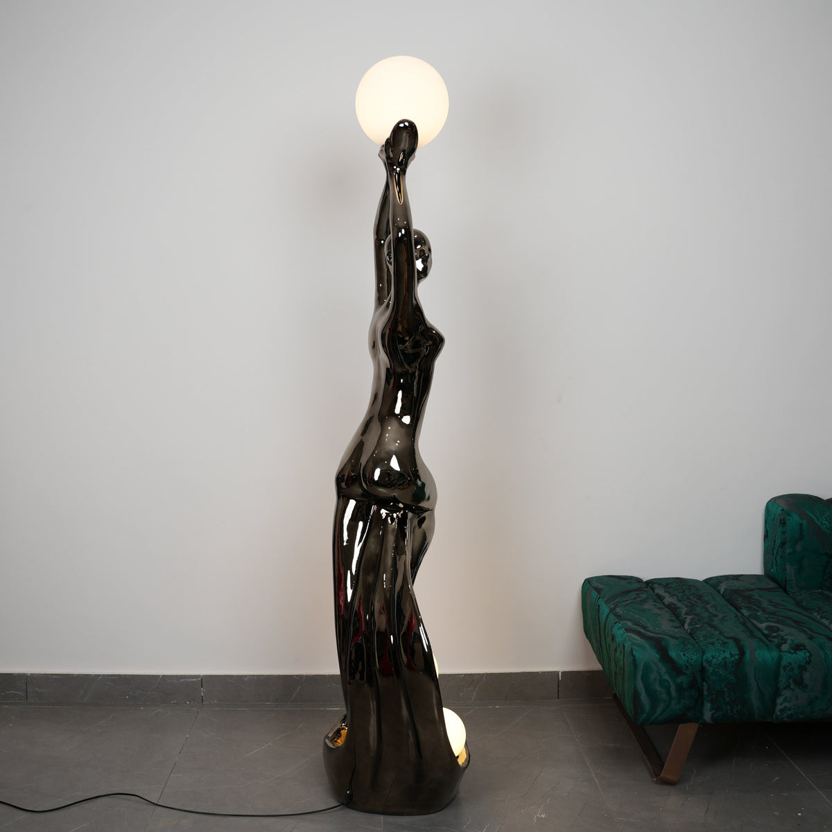Black floor lamp shaped like a woman with a round light bulb on a gray floor.