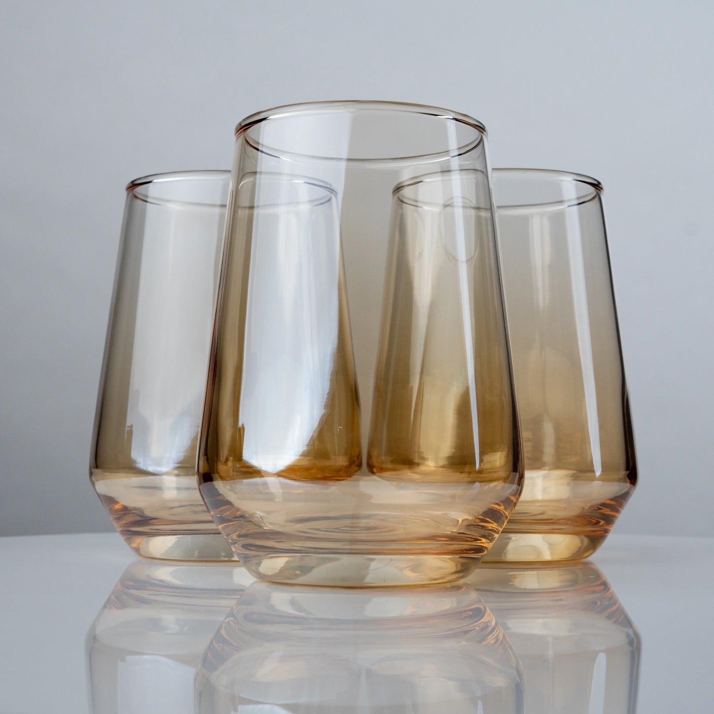 Set of two amber-tinted modern drinking glasses with tapered silhouette on reflective surface; elegant glassware for beverages