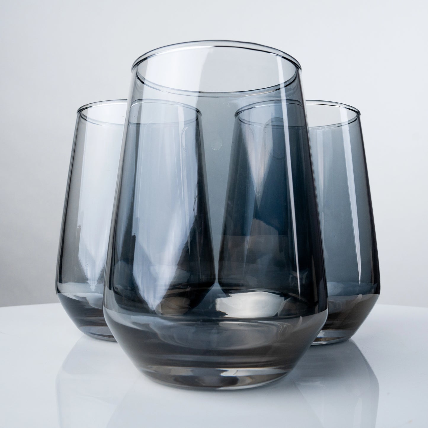 Set of smoky grey 410 ml drinking glasses with modern tapered silhouette on a reflective surface; stylish premium glassware