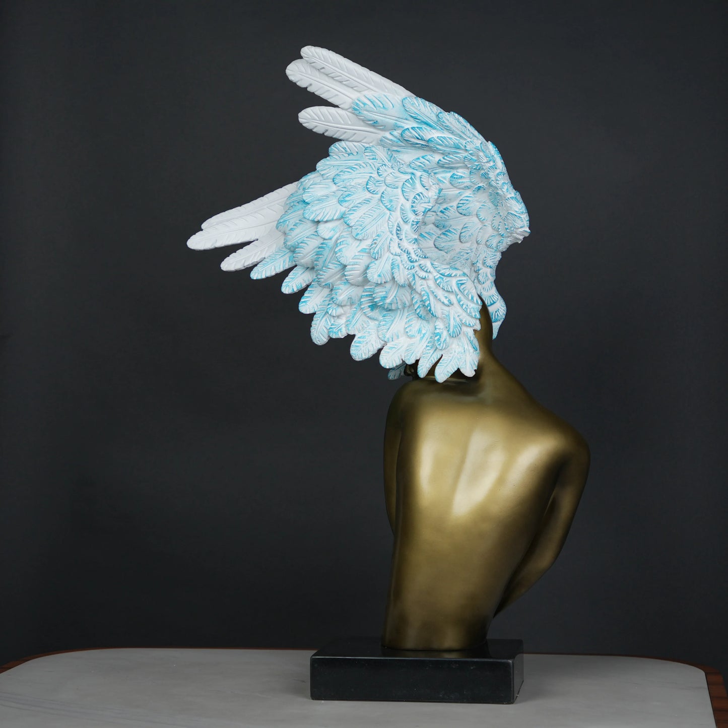 Gold-bodied woman sculpture with large white and blue feathered wings on a black base — luxury artistic décor piece.