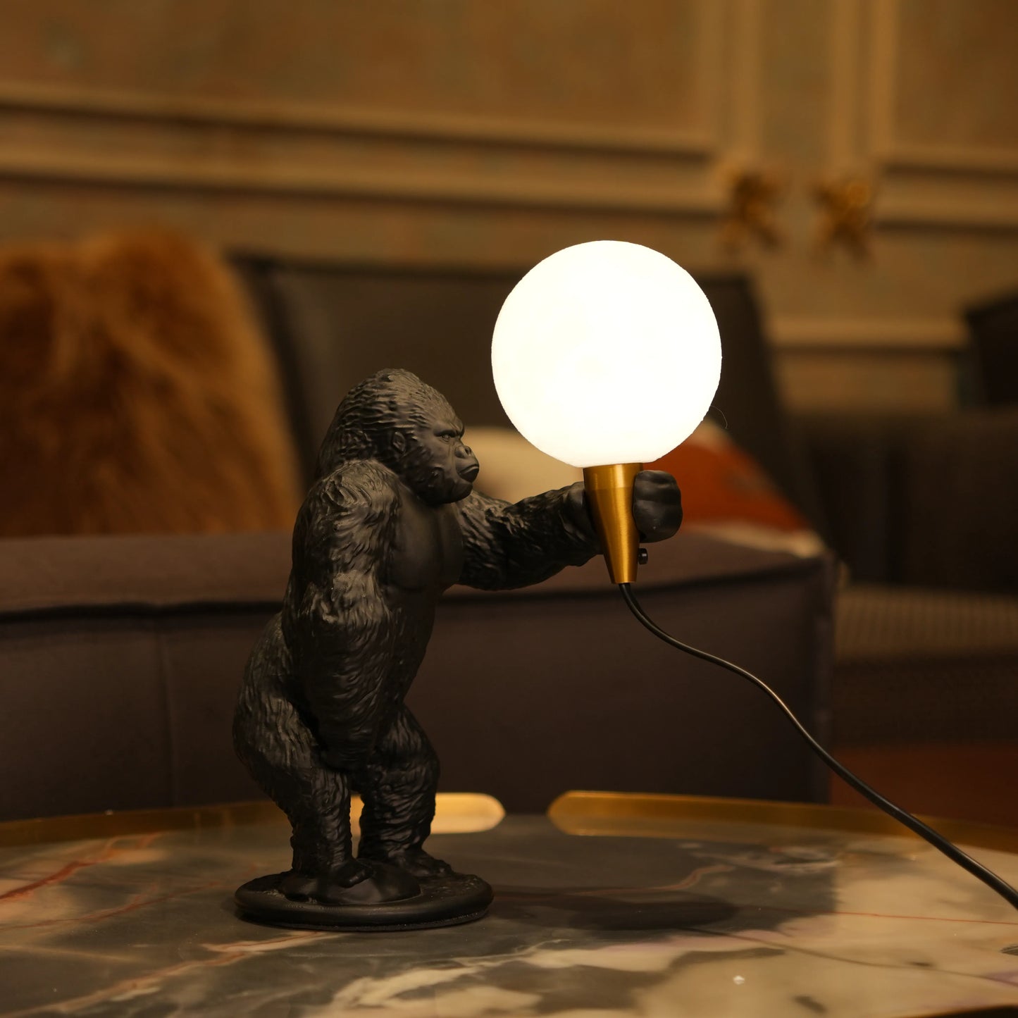 Black gorilla sculpture lamp holding a warm glowing orb with a gold lamp holder on a round black base.