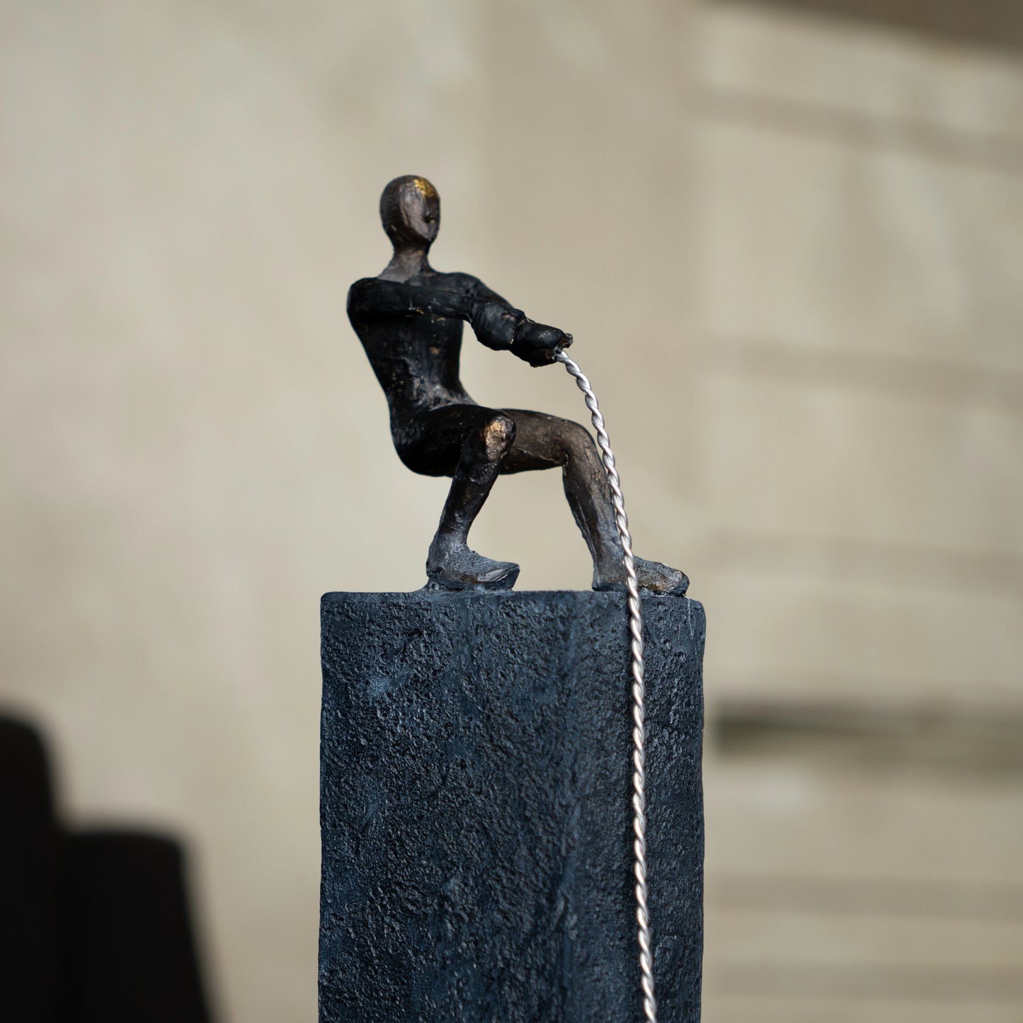 Bronze pulling figure sculpture on textured charcoal stone base with hanging weight.