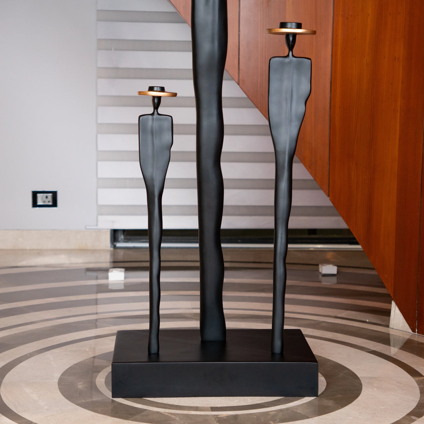 Tall matte black resin sculpture of three elongated human figures with bronze hats — Ethereal Harmony Sculpture by Ghar Art, handcrafted luxury decor symbolizing unity and balance.