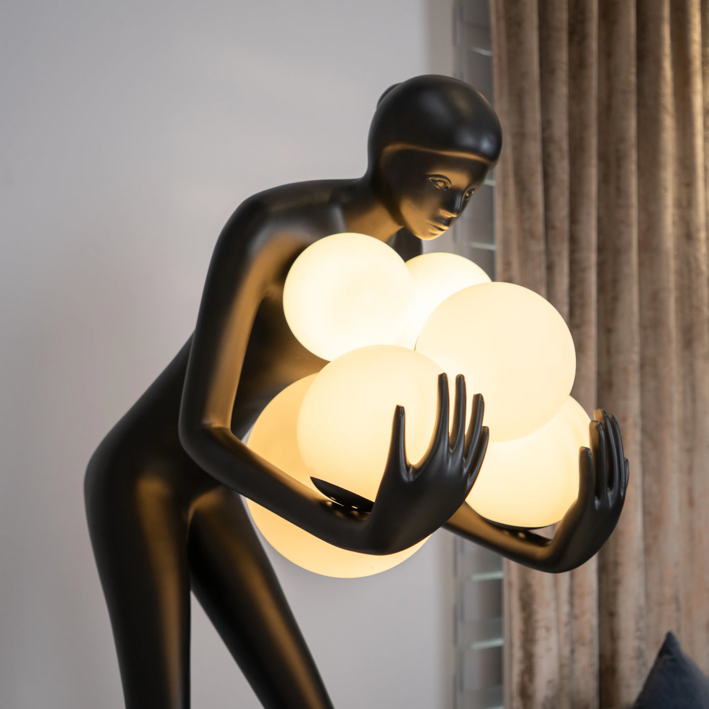 Tall matte black human sculpture holding glowing white orbs