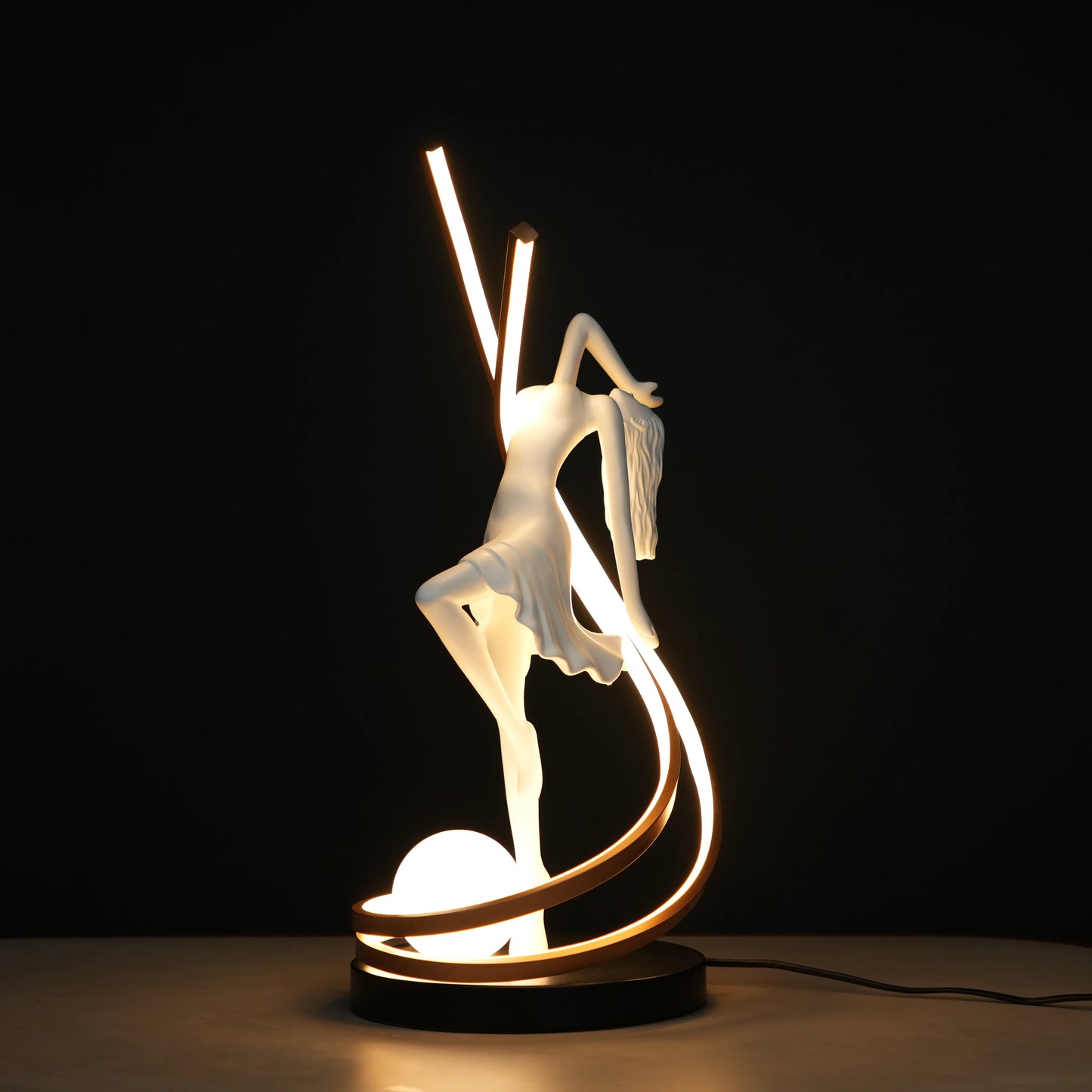 Small white sculpture lamp of a dancing woman with sweeping LED arcs and a glowing orb on a black base.