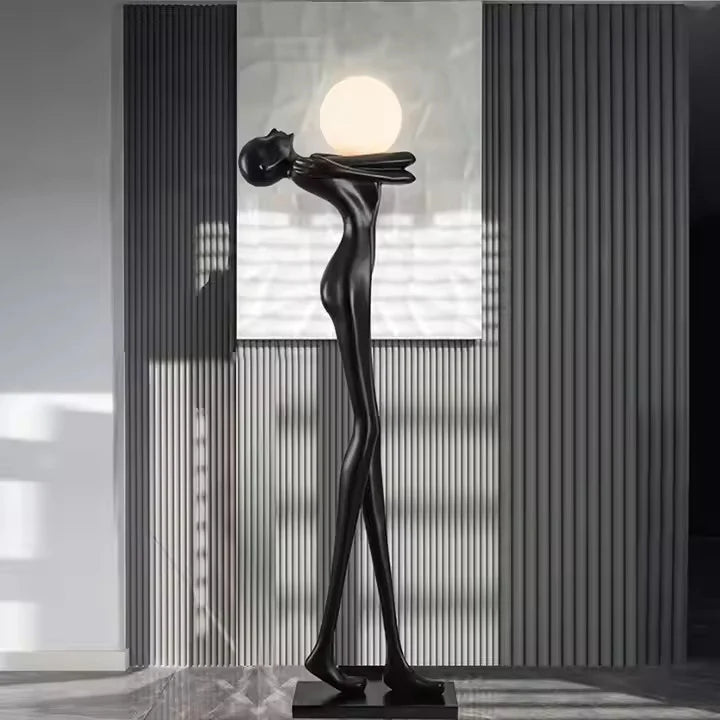 Tall matte black human sculpture floor lamp holding a glowing orb in a modern interior setting.”