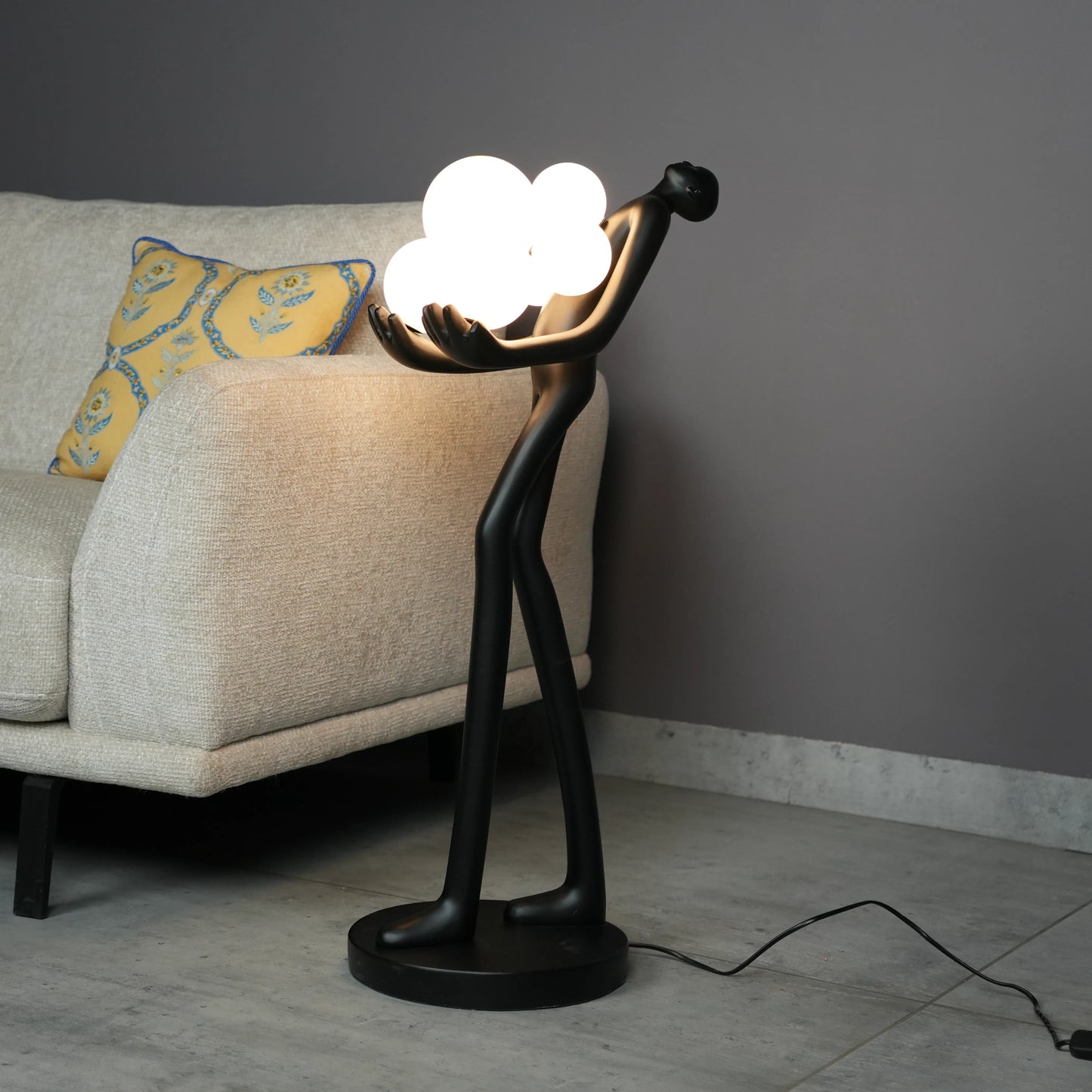 Black abstract human sculpture floor lamp holding glowing cloud-shaped warm white globes