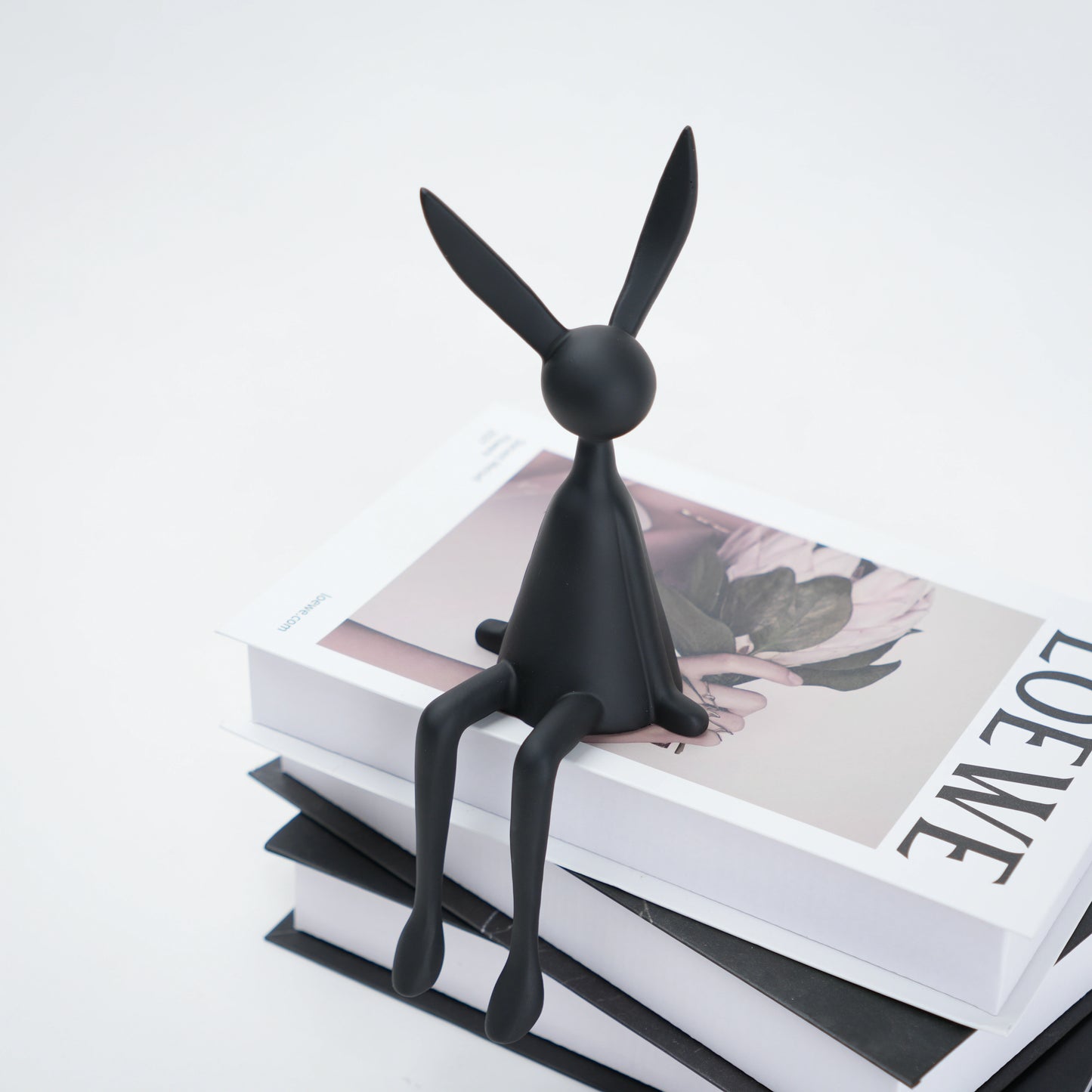 Black rabbit-shaped object on a stack of books with a white background