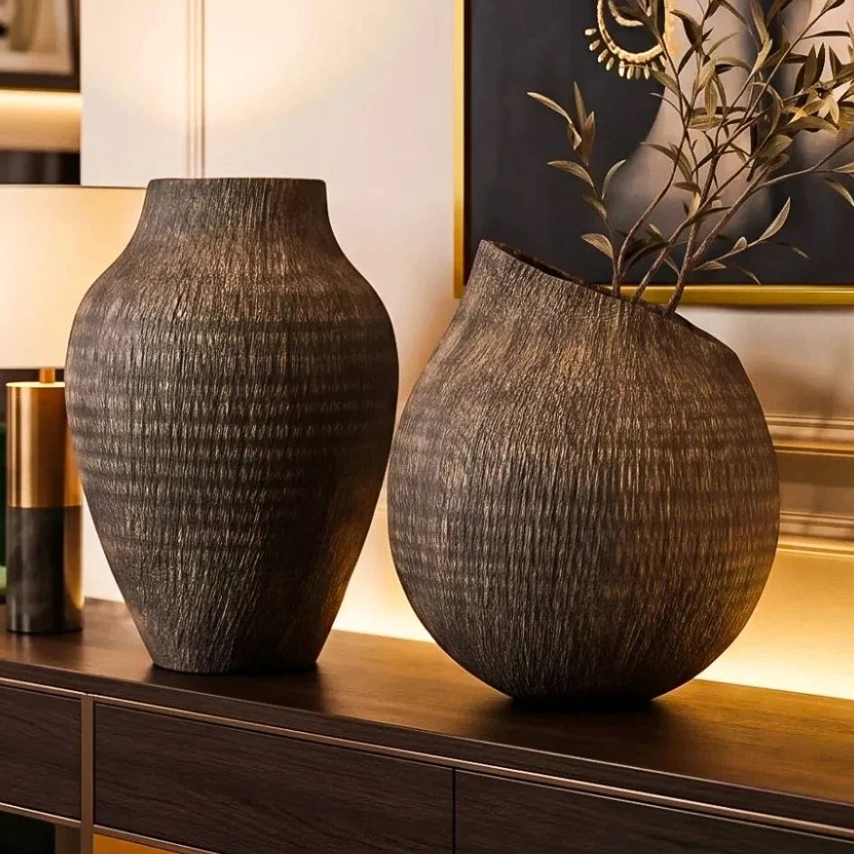 Two dark brown textured ceramic vases displayed on a wooden console table in a modern, warm-toned interior setting.