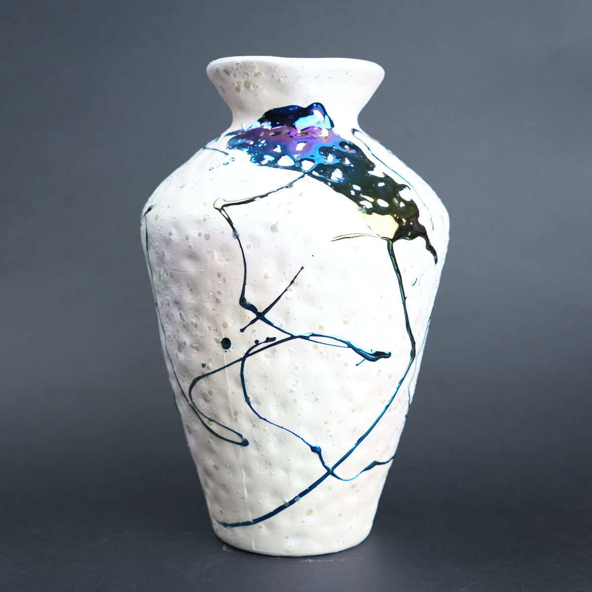 White ceramic vase with abstract black and blue designs on a gray background