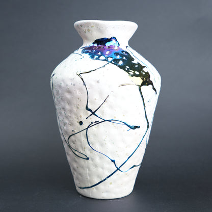 White ceramic vase with abstract black and blue designs on a gray background