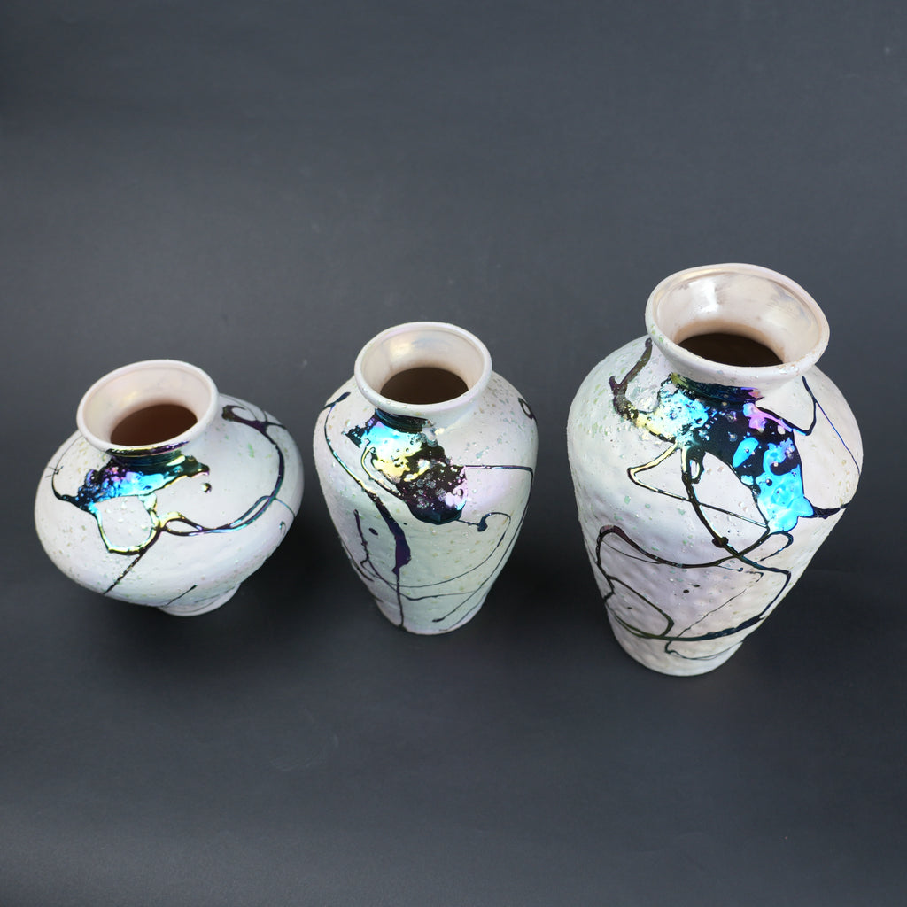 Three ceramic vases with abstract designs on a dark background