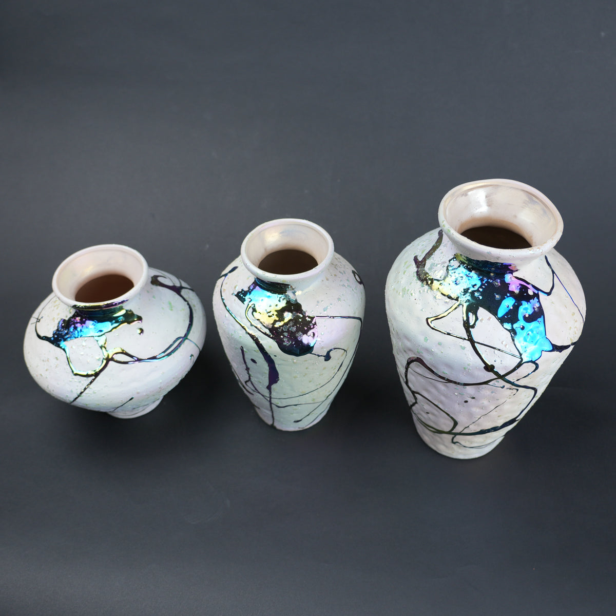 Three ceramic vases with abstract designs on a dark background