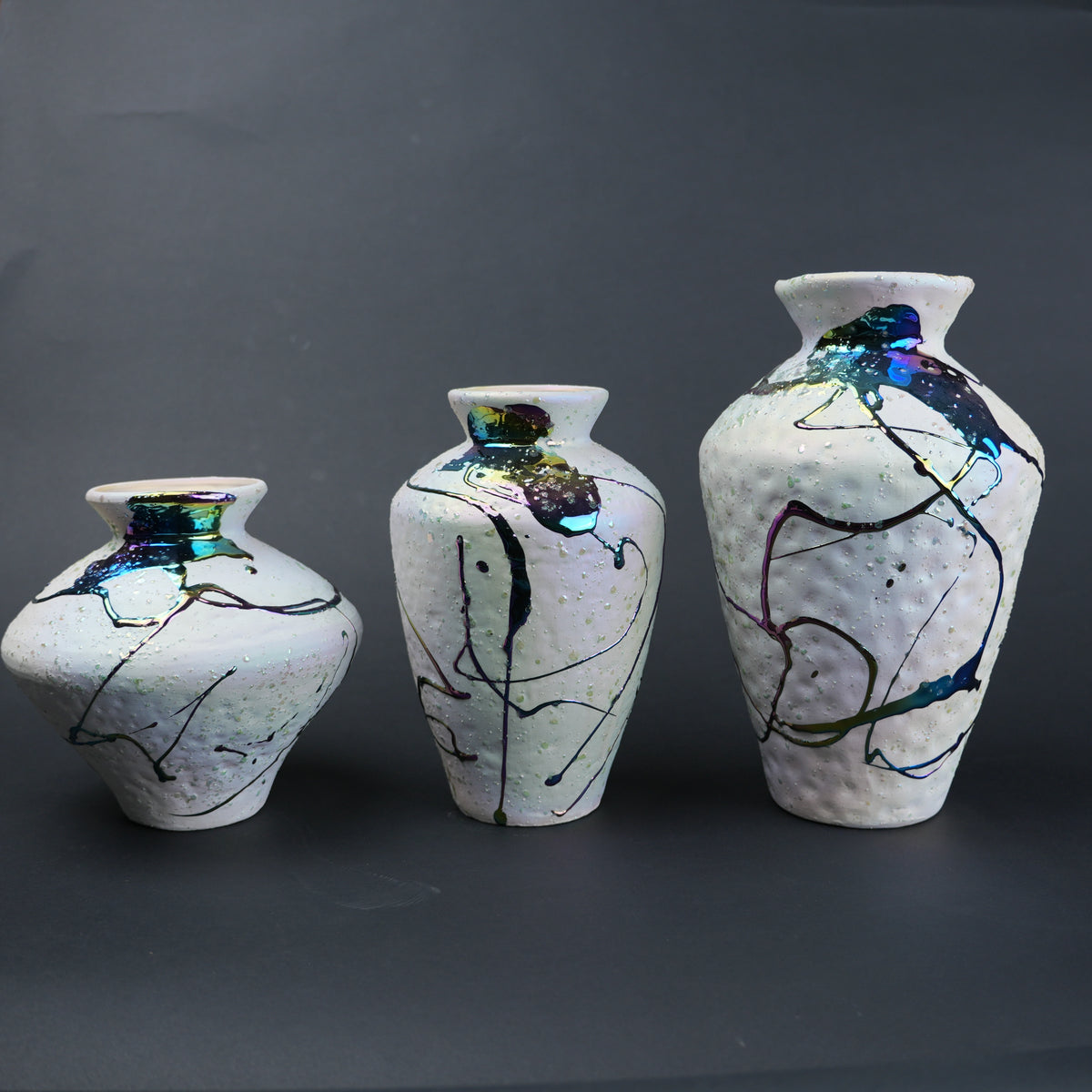 Three ceramic vases with abstract designs on a dark background