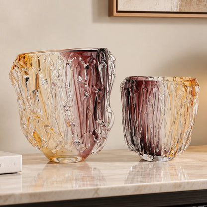 Two decorative hand-blown glass vases with a textured, tree-bark-like pattern in amber, gold, and deep burgundy tones, displayed on a polished marble console table in a modern interior setting.
