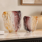 Two decorative hand-blown glass vases with a textured, tree-bark-like pattern in amber, gold, and deep burgundy tones, displayed on a polished marble console table in a modern interior setting.