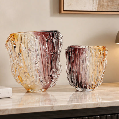 Two decorative hand-blown glass vases with a textured, tree-bark-like pattern in amber, gold, and deep burgundy tones, displayed on a polished marble console table in a modern interior setting.