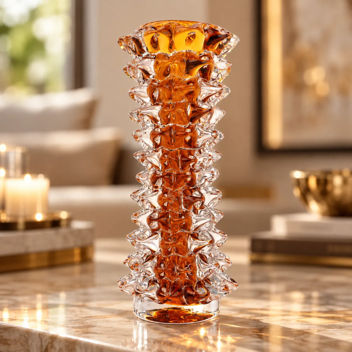 A tall, sculptural clear glass vase with a textured, layered honeycomb-like pattern and a warm amber tint near the top, displayed on a polished marble table in a softly blurred living room setting.