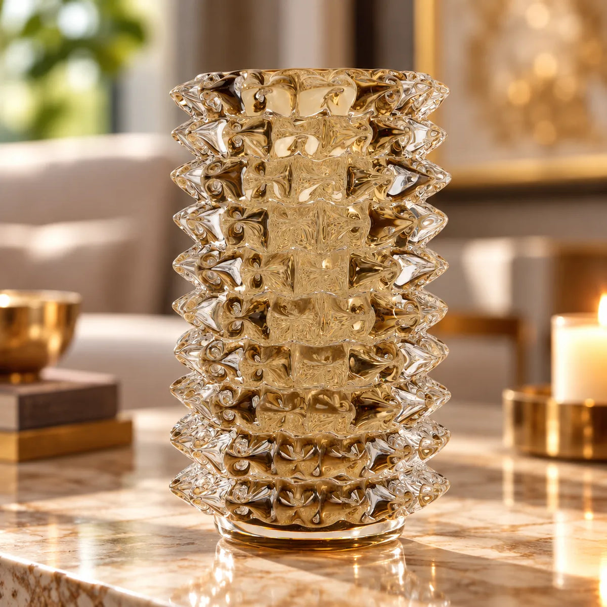 A clear textured glass vase with a geometric, faceted pattern and a fluted base, displayed on a polished marble table in a warm, softly blurred living room setting.