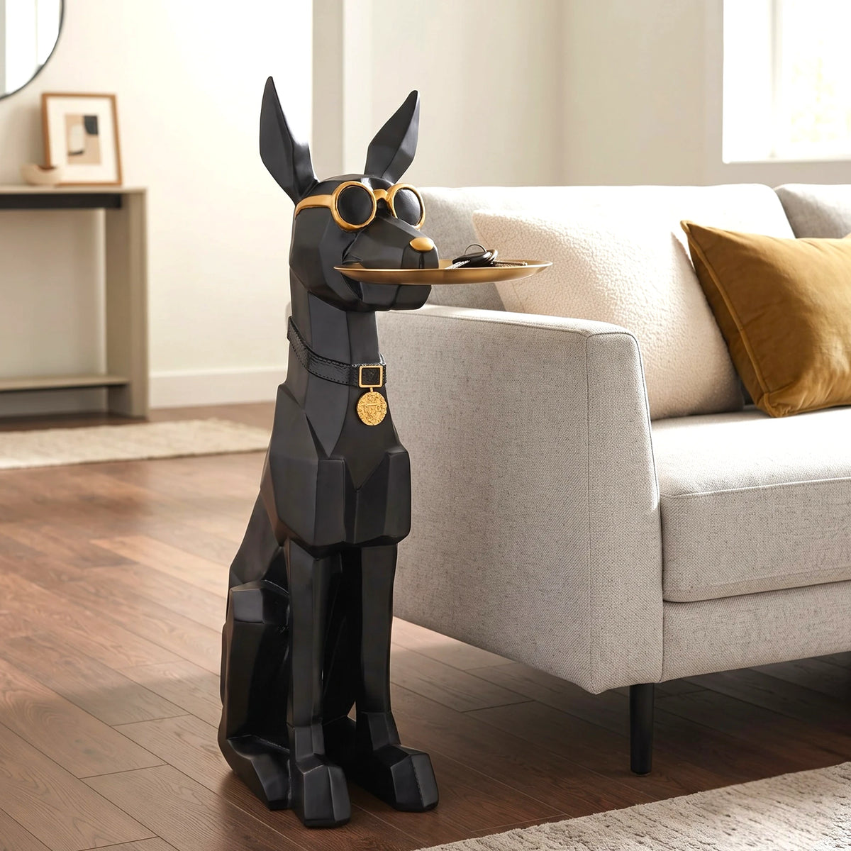 A black geometric dog-shaped floor lamp or decorative stand with gold-tone glasses and collar details, holding a tray in its paws, placed beside a light beige sofa on a wood floor.