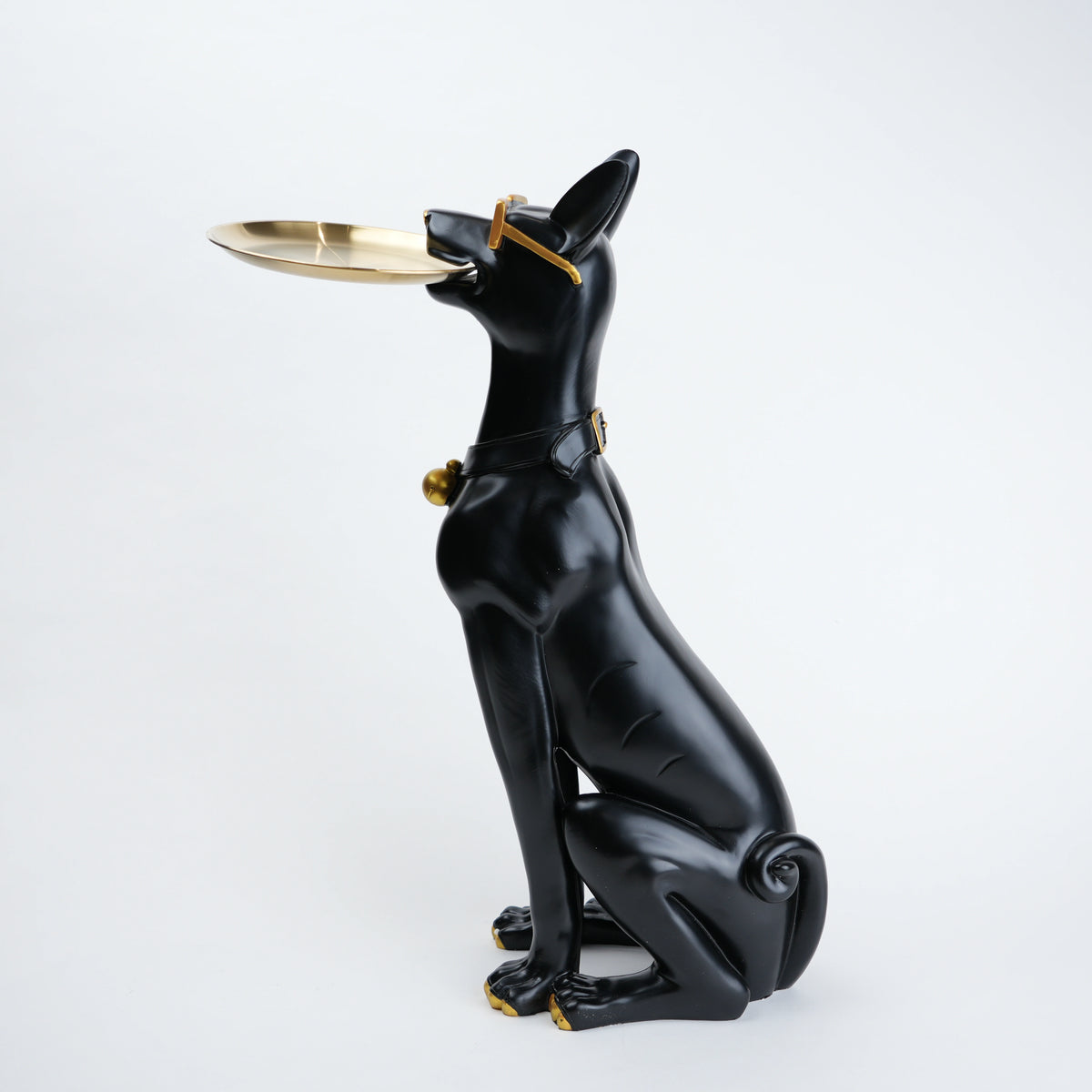 A glossy black dog figurine sitting upright and holding a small gold tray in its mouth, with gold accents on the collar and tray, photographed against a clean white background.
