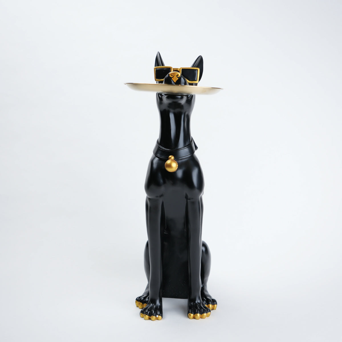A glossy black cat figurine wearing a beige hat with gold trim and sunglasses, plus a black collar with a gold bell, posed against a clean white background.