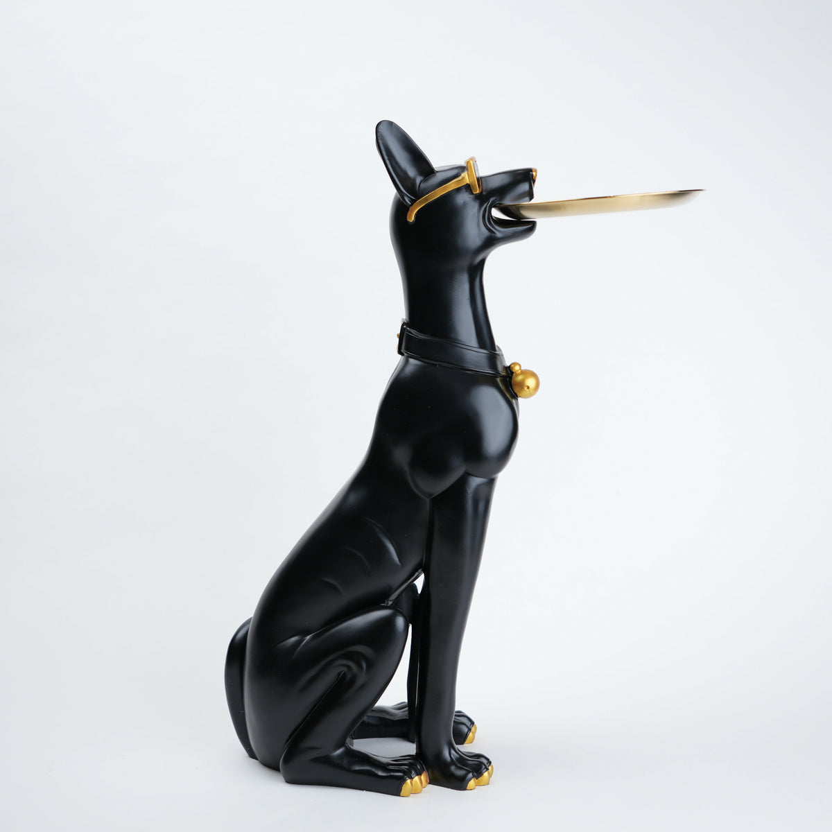 A glossy black cat figurine in a seated pose, holding a gold-colored sword in its mouth, with small gold accents on its collar and paws, set against a plain light gray background.