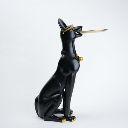 A glossy black cat figurine in a seated pose, holding a gold-colored sword in its mouth, with small gold accents on its collar and paws, set against a plain light gray background.
