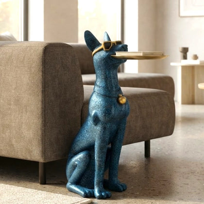 A blue metallic dog-shaped decorative table holding a tray in its mouth, styled in a modern living room next to a gray sofa.