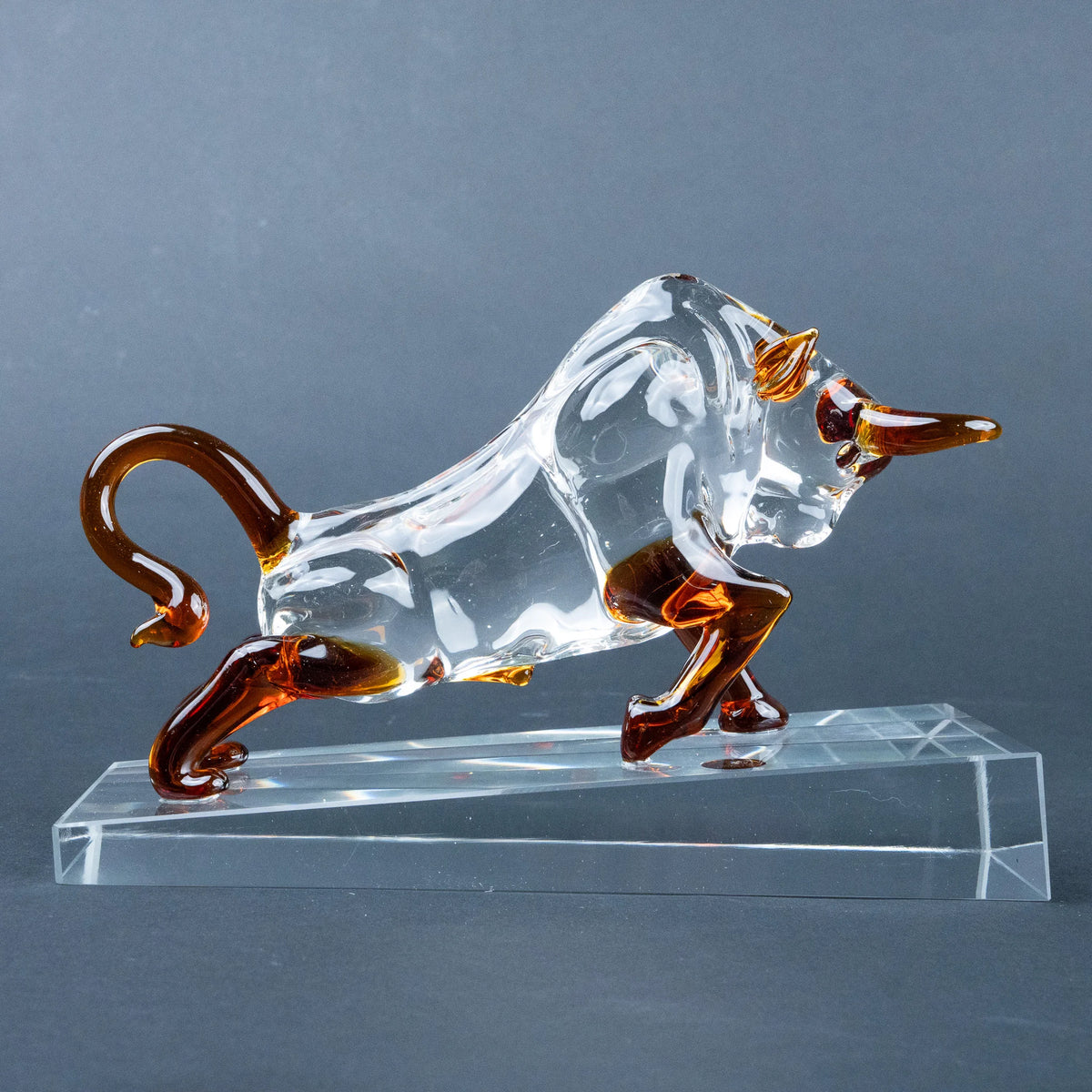 A transparent glass bull figurine with amber-brown accents on its horns, legs, and tail
