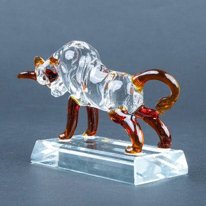 A clear glass bull figurine with amber-brown legs, tail, and horns, standing on a transparent rectangular glass base.