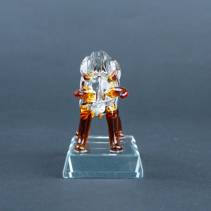 A small clear glass figurine of a seated figure with amber-brown legs and red accents