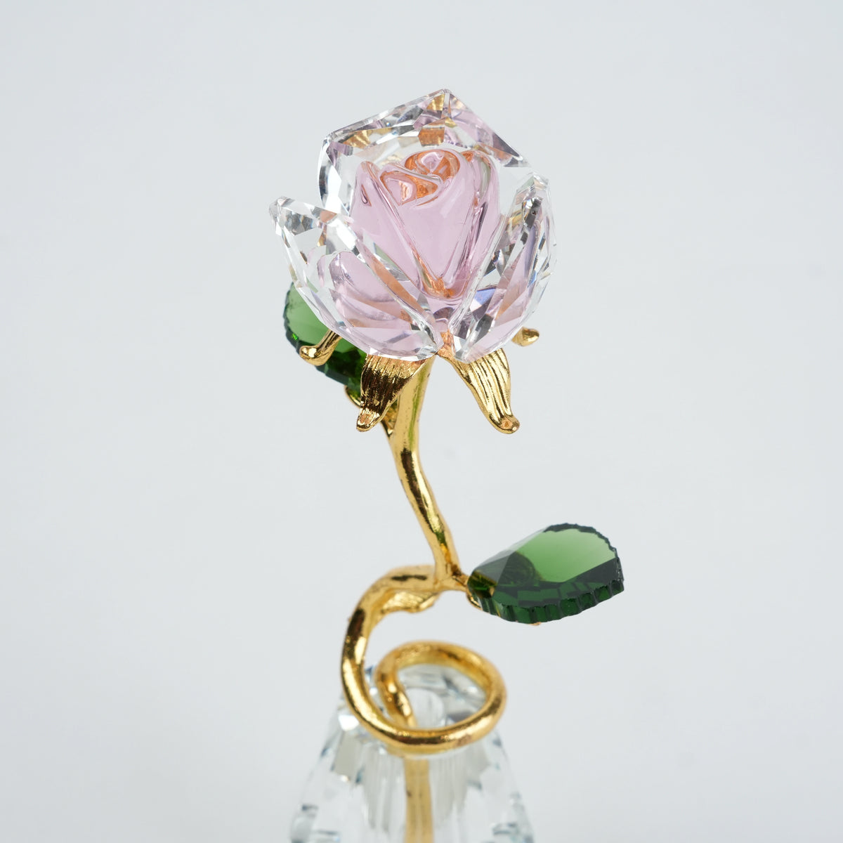Crystal rose with gold stem and green leaves on a light gray background