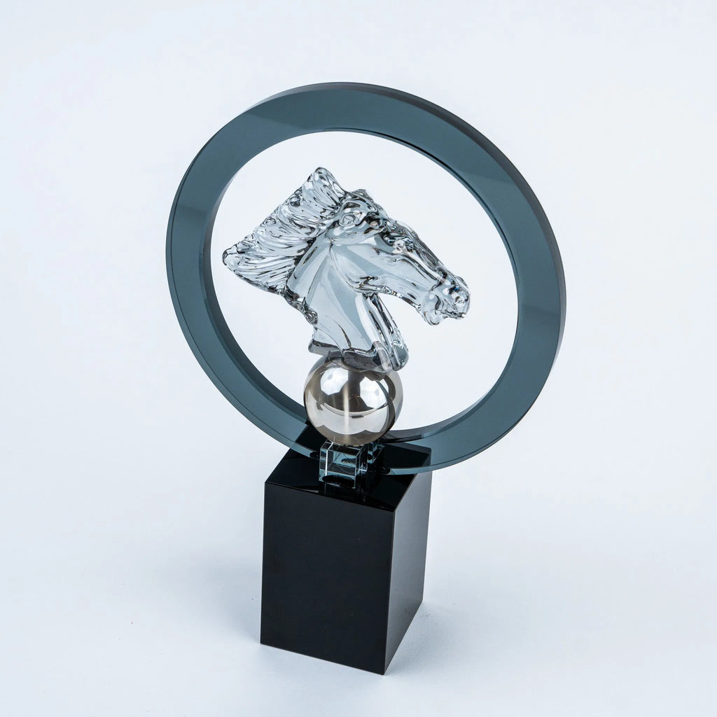 A clear acrylic horse head trophy sculpture mounted on a black rectangular base, with a transparent circular ring behind it, photographed on a light gray studio background.