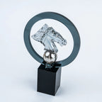 A clear acrylic horse head trophy sculpture mounted on a black rectangular base, with a transparent circular ring behind it, photographed on a light gray studio background.