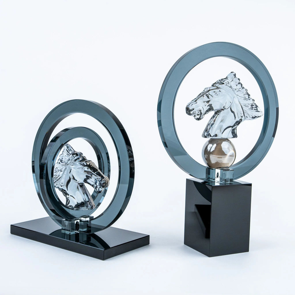 Two modern horse-head ring sculptures displayed on a clean white studio background. One smaller version sits on a glossy black rectangular base, while the larger version stands on a glossy black pedestal with a metallic sphere.