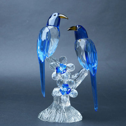 A crystal and glass figurine of two blue-and-white birds perched on a clear flowering branch with blue flower accents,