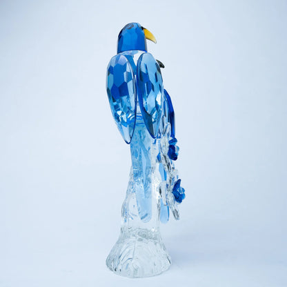 A decorative glass sculpture of a blue bird perched on a clear, faceted base, photographed