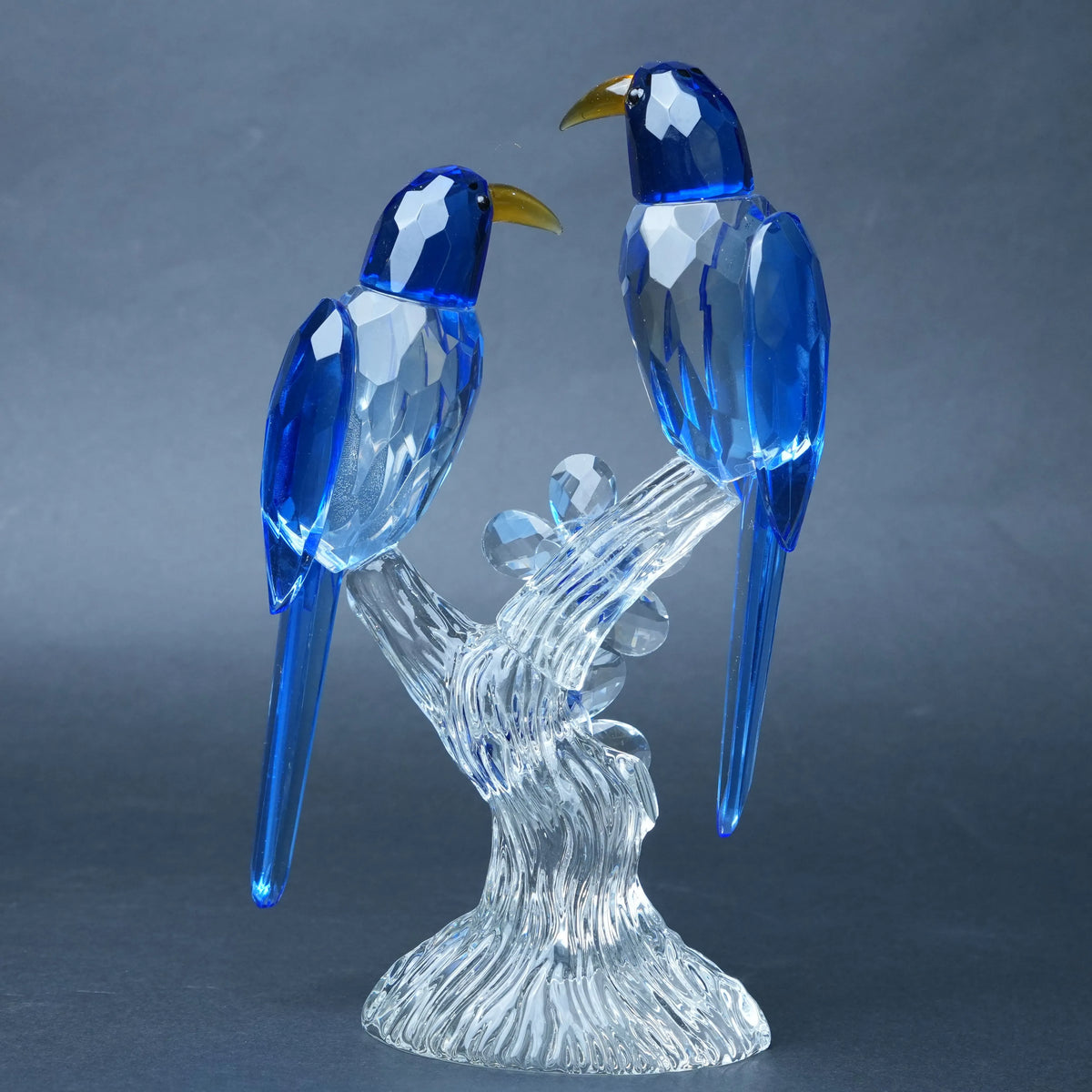 A decorative crystal figurine of two blue birds perched on a clear, faceted branch and base