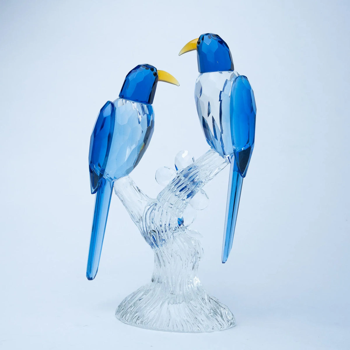 A decorative figurine of two blue birds perched on a clear glass branch and base, photographed