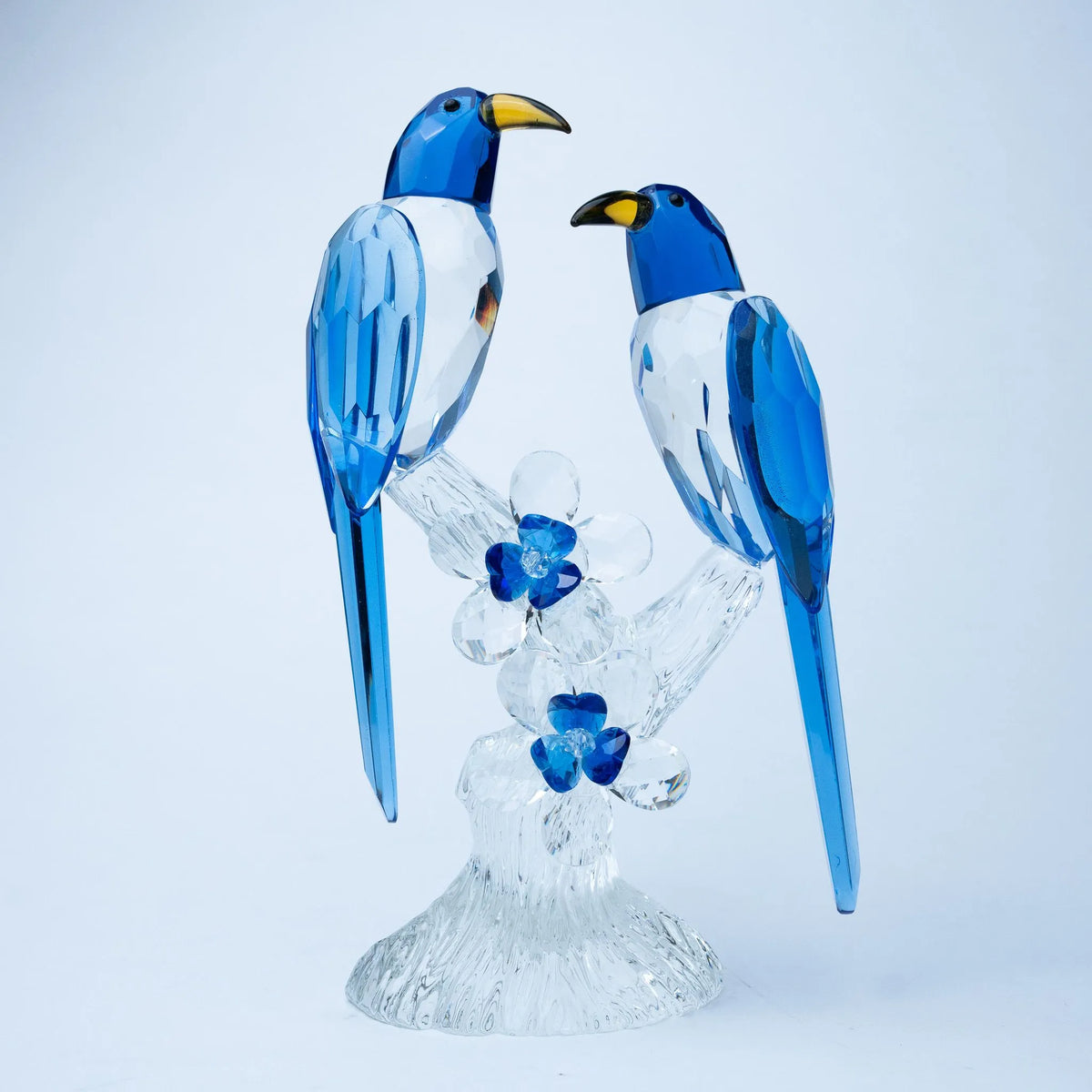 A decorative glass figurine of two blue-and-white birds perched on a clear glass branch with small blue flowers, photographed 