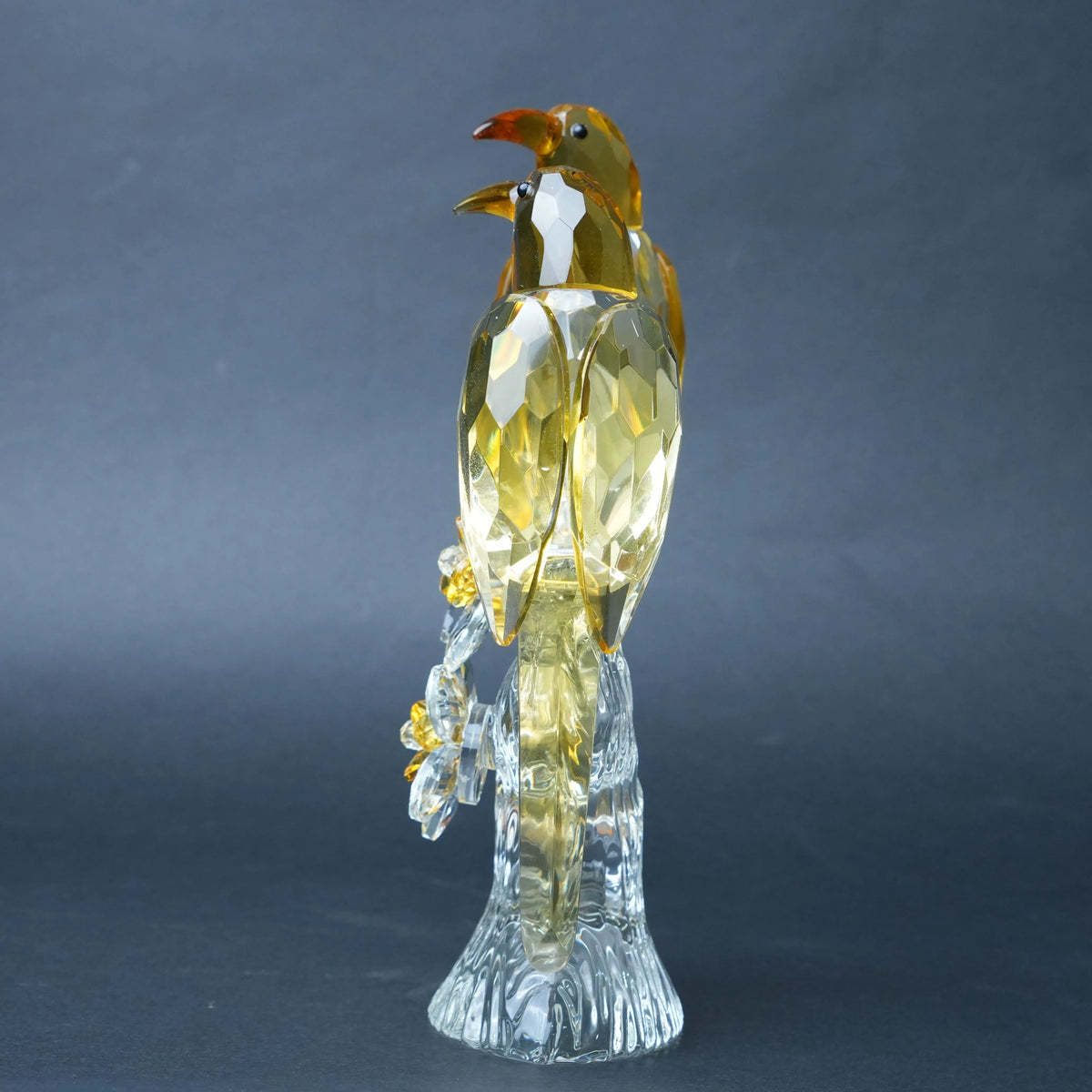 A faceted crystal bird figurine with a golden-yellow body and a clear transparent base.