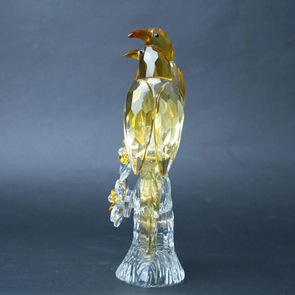 A faceted crystal bird figurine with a golden-yellow body and a clear transparent base.