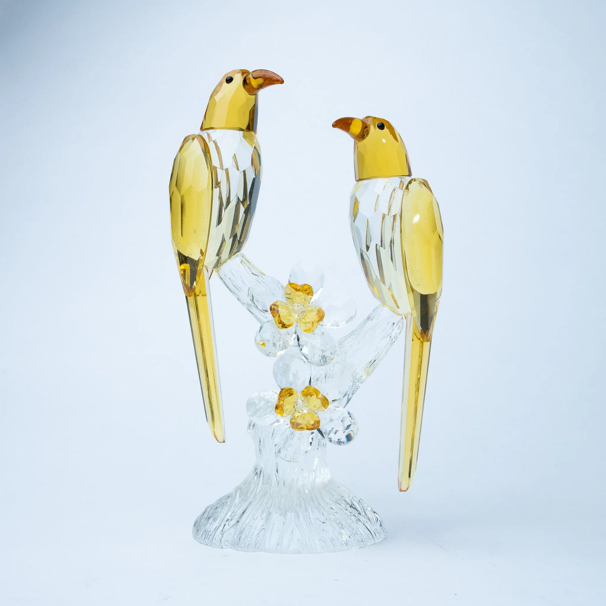 A decorative figurine of two yellow birds perched on a clear crystal branch with small yellow flowers
