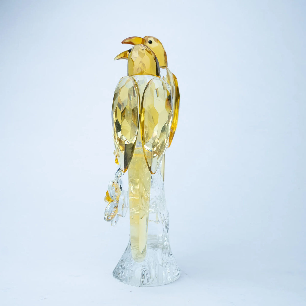 A decorative bird figurine made of faceted transparent and translucent materials, with a yellow-gold bird body and wings mounted on a clear crystal-like base.