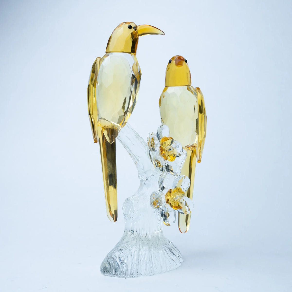 A decorative figurine of two golden birds perched on a clear glass branch with small yellow flowers