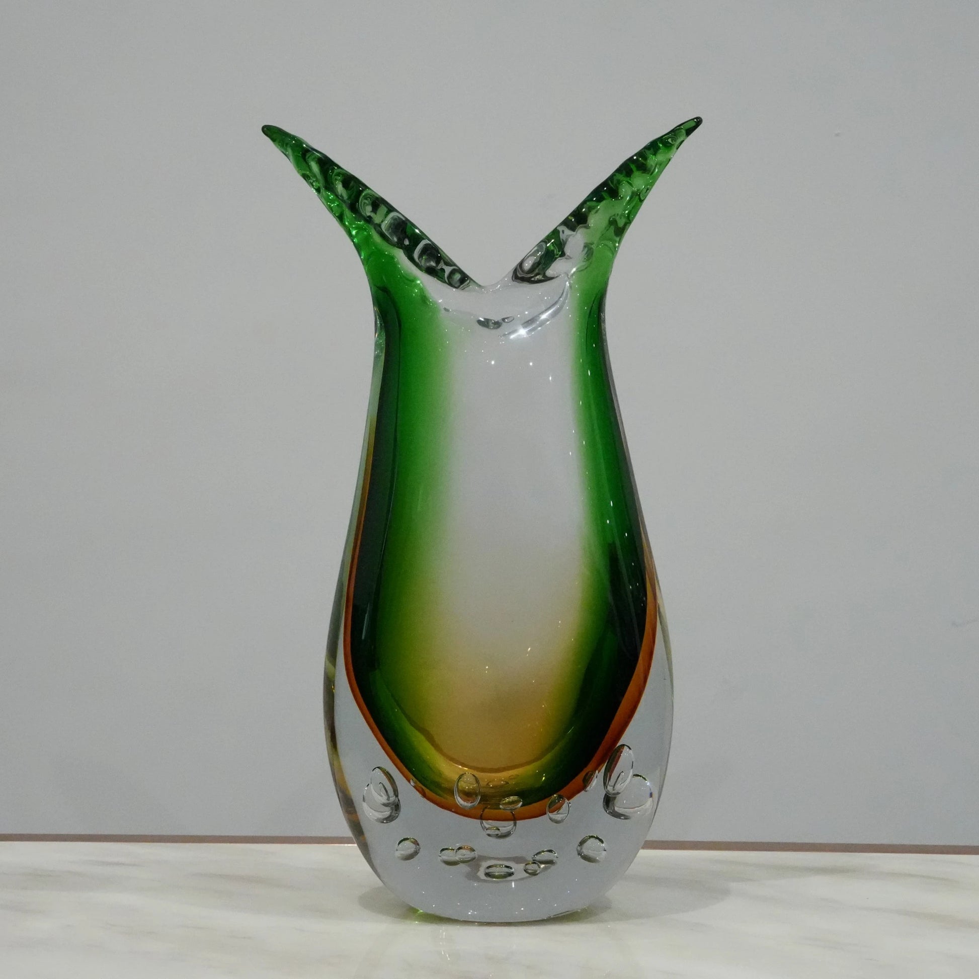 Handblown artistic glass vase with flowing horn silhouette, bubble detailing and green amber gradient finish for luxury modern decor