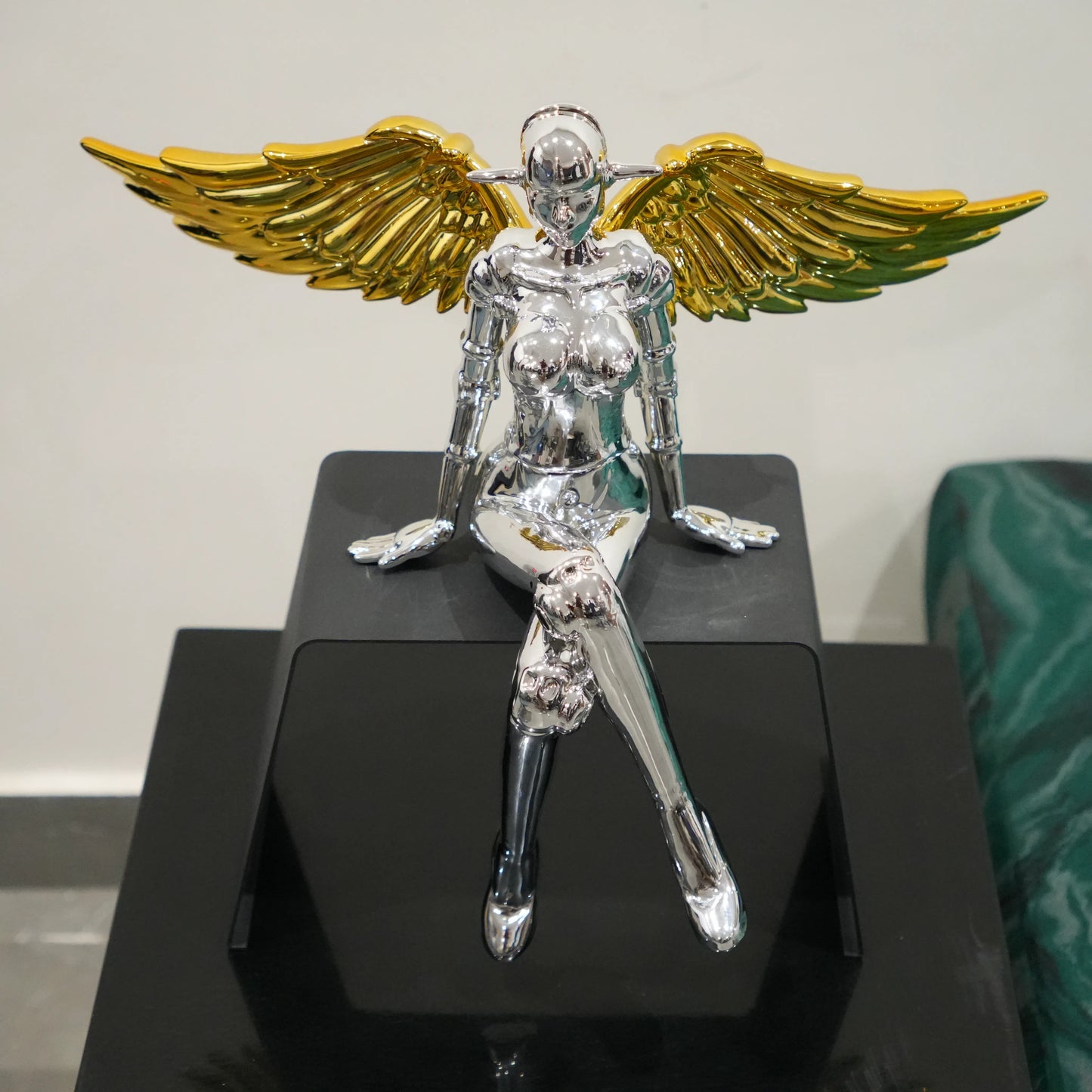 Metallic sculpture of a winged figure with gold wings on a black platform.