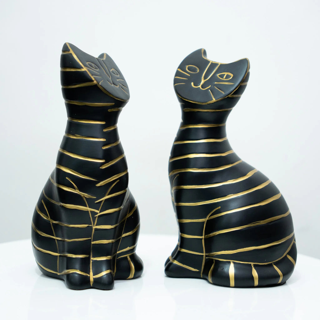 Two black cat figurines with gold stripes, one facing left and one facing right, displayed on a white surface against a white background.
